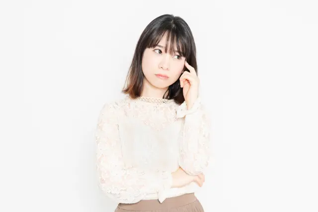 白背景の前に立って、悩んでいる、レースのブラウスを着た若い女性